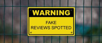 Yellow warning sign on a fence stating : Warning, Fake reviews spotted.